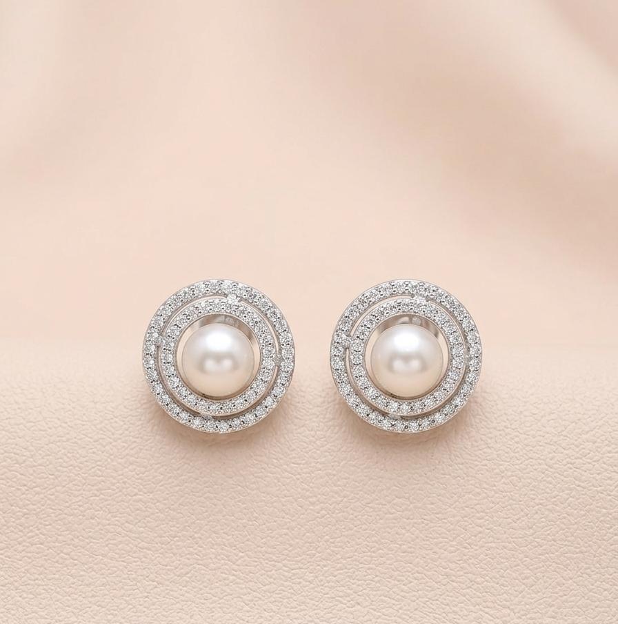 Pair of pearl earrings with diamond accents on a light pink background