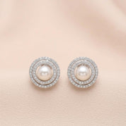 Pair of pearl earrings with diamond accents on a light pink background
