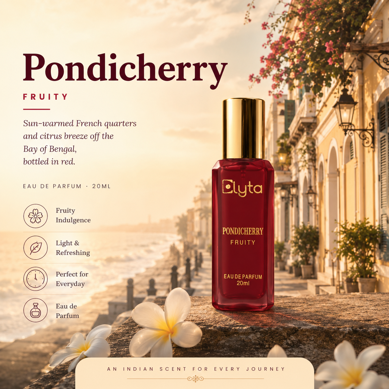 A 20ml bottle of Elyta Pondicherry Fruity Eau de Parfum displayed on a stone ledge in a scenic, sunlit street setting. The bottle is deep red with a shiny gold cap, and the background features warm-toned colonial buildings, hanging pink flowers, and white plumeria flowers.
